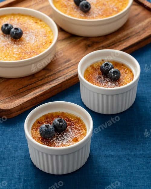 Preview: Creme brulee in lot of ramekin on wooden tray on dark linen tablecloth. Close up cream dessert