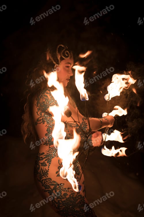 Preview: A seductive woman performer dancing at night with sticks of fire against the snow
