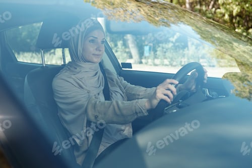 Preview: Young businesswoman in hijab holding by steering wheel while driving car