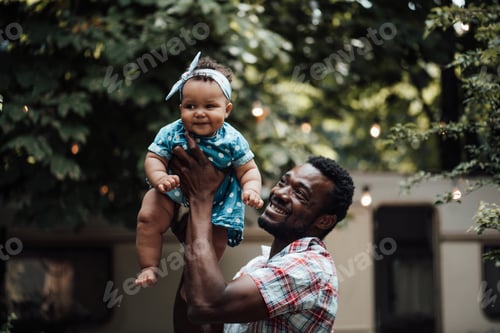 Preview: Smiling Man Holding an Infant Outdoors in Daytime
