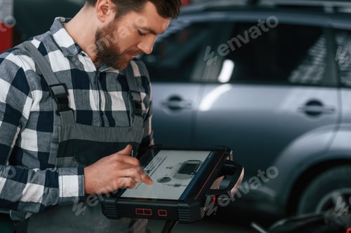 Preview: Graphic information is on the tablet. Man in uniform is working in the auto salon