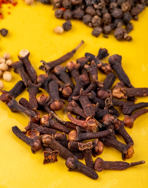 Preview: side view of a heap of clove spice on yellow background
