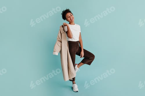 Preview: Full length view of gorgeous black woman in pants standing on one leg. Studio shot of smiling afric