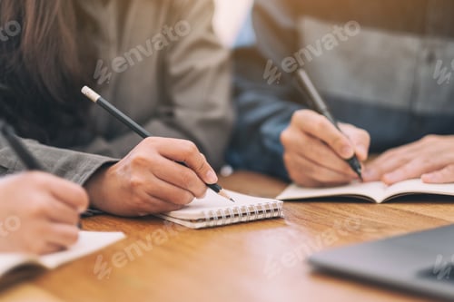 Preview: Closeup image of people writing on blank notebook together on wooden table