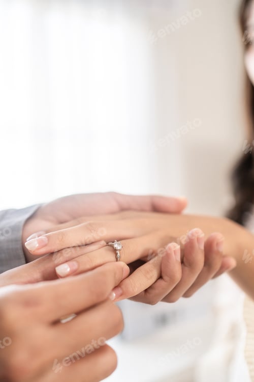 Preview: Close up of romantic groom puts wedding diamond ring on bride's finger.