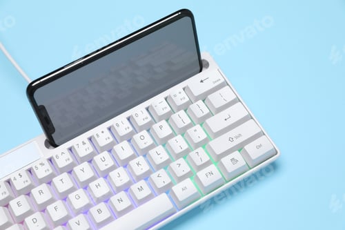 Preview: Modern white keyboard with RGB lighting and smartphone on light blue background, closeup
