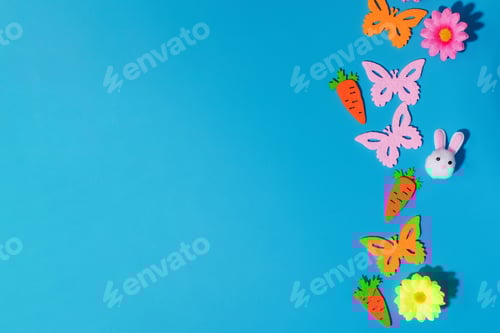 Preview: Easter decorations with felt butterflies, carrots, and flowers on blue. Copy space