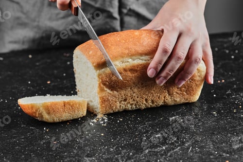 Preview: Woman cutting bread with knife on dark desk