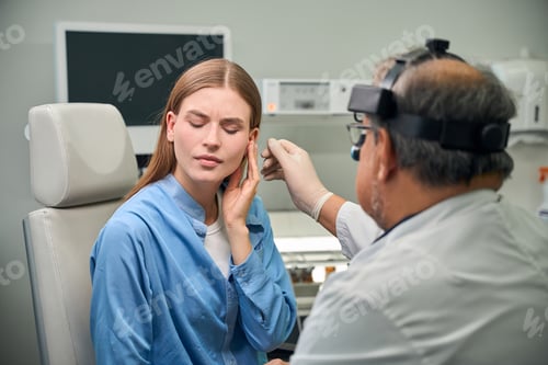 Preview: Elderly male doctor examines patient's ear closely