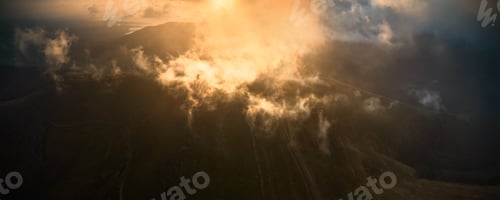 Preview: Aerial view of mountain landscape at sunrise, with sun golden rays piercing through mist and clouds