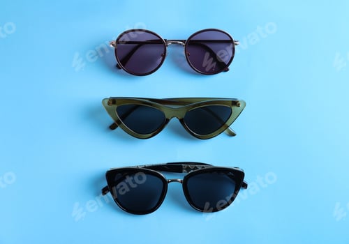Preview: Many stylish sunglasses on light blue background, flat lay