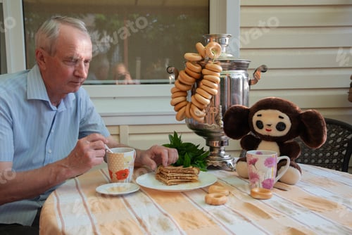 Preview: An elderly man enjoys a traditional Russian tea party with a samovar, pretzels, svegomo pancakes