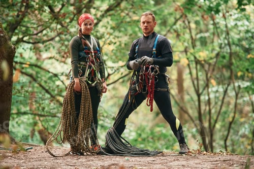 Preview: Standing and posing. Man and woman doing climbing in forest with use of safety equipment