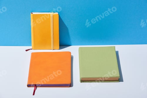 Preview: multicolored notebooks on white desk and blue background