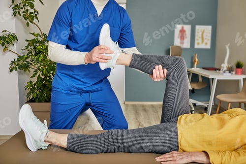 Preview: Physiotherapist treating leg injury on a senior woman lying down