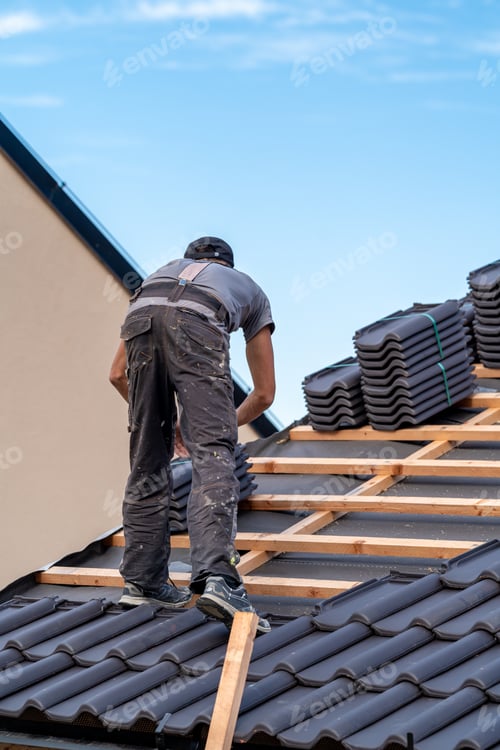 Preview: construction worker installs a fired ceramic tile on the roof of family house
