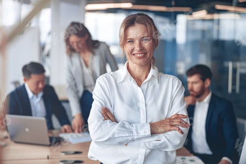 Vista previa: Retrato de hermosa mujer de negocios madura sonriente con sus colegas en segundo plano en la oficina