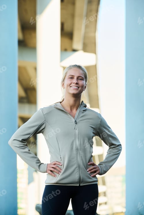 Preview: Happy young blond female athlete with toothy smile standing in urban environment