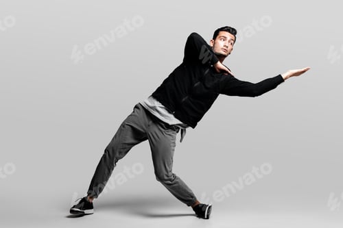 Preview: Dark-haired stylish young man wearing a black sweatshirt and gray pants is dancing street dances