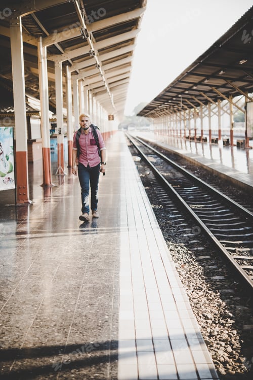 Preview: Young hipster man waiting on the station platform with backpack. Travel concept.