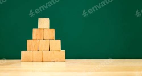 Preview: Pyramid shape build from wood cube on wooden table with green blackboard