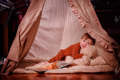 Preview: Cozy winter vibes. Little toddler child in pajama read book together with soft furry teddy at home