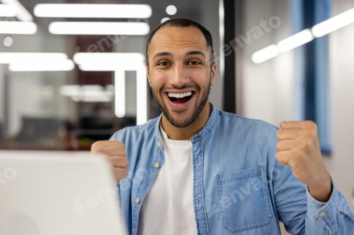 Preview: Close-up portrait of a happy young hispanic man sitting in a modern office in front of a laptop and