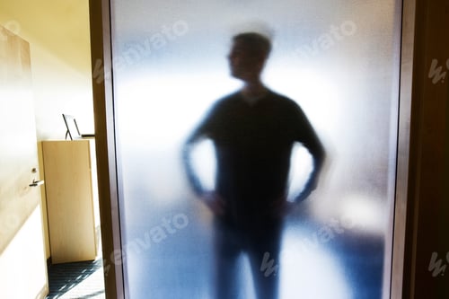 Preview: An abstract silhouette of a businessman distorted through a glass wall in an office.