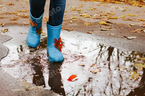Preview: Teenager girl wearing blue rain boots jumping into a puddle on rainy autumn day. Closeup. N