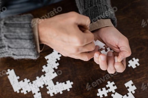 Preview: cropped view of senior man suffering from parkinsonism and holding elements of jigsaw puzzle in