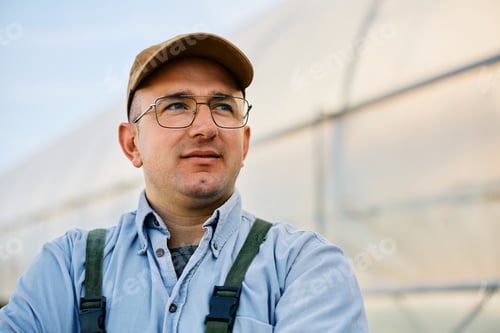 Preview: Small business owner in front his greenhouse looking away.