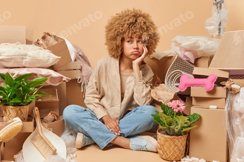 Preview: Moving to own home. Upset displeased woman sits in lotus pose on floor in empty room with cardboard