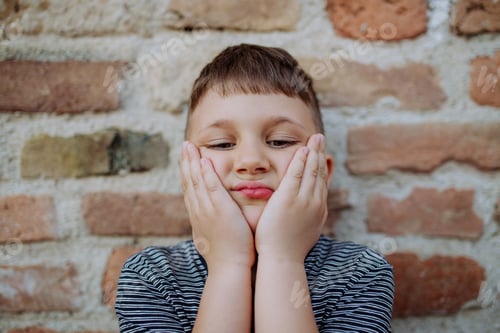 Preview: Little boy standing by brick wall and making funny faces in street summer.