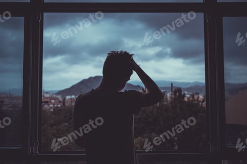 Preview: Boy feeling depressed in front of the window under the clouded sky