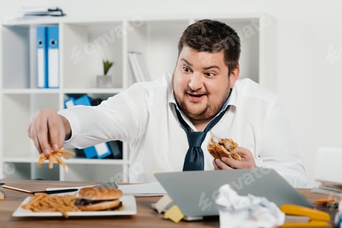 Preview: overweight businessman eating hamburgers and french fries in office