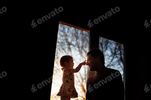 Preview: Silhouettes of a little girl with dad at the window in the sunbeams.