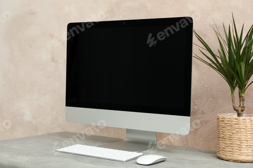 Preview: Workplace with computer and plant on wooden table. Light brown background