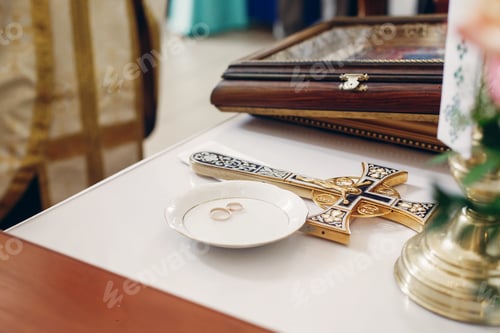 Preview: Couple of golden wedding rings on white plate near christian cross