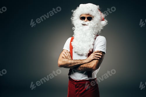 Preview: serious santa claus in sunglasses standing with crossed arms isolated on grey background