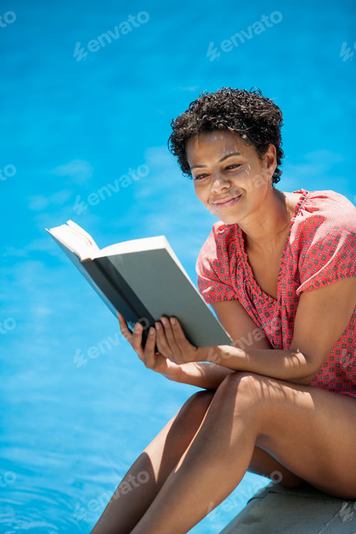 Preview: A woman sitting at a swimming pool, reading a book.
