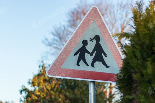 Preview: red triangular road sign "beware, children go to school" against the backdrop of trees