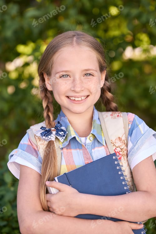 Preview: Smiling caucasian girl child with braided hair holding notebook outdoors