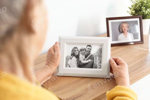 Preview: Elderly woman with framed family portrait at home