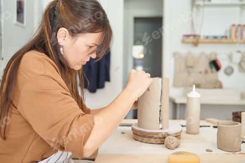 Preview: Female potter making handmade piece with clay while working in pottery studio.
