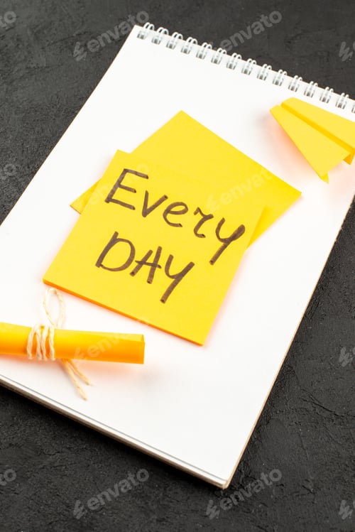 Preview: bottom view every day written on sticky note scroll sticky note on spiral notepad on dark background