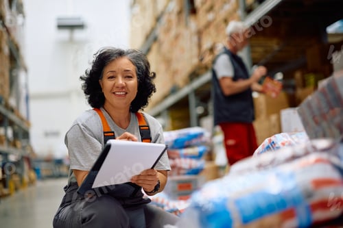 Preview: Happy female worker at distribution warehouse and looking at camera.