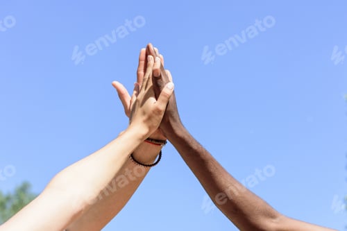 Preview: cropped shot of friends giving high five to each other against blue sky
