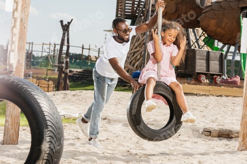 Preview: african american father and daughter on tire swing having fun on playground