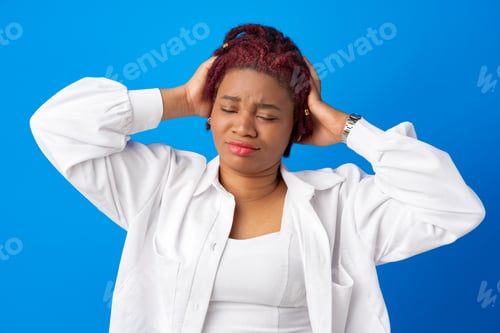 Preview: Young afro woman suffering headache against blue background
