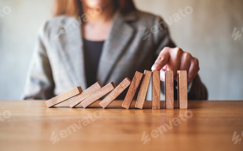 Preview: a businesswoman's finger try to stopping falling wooden dominoes blocks